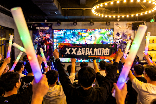 社区玩家聚集在线下观赛点，手举荧光棒和应援横幅共同为支持的战队加油